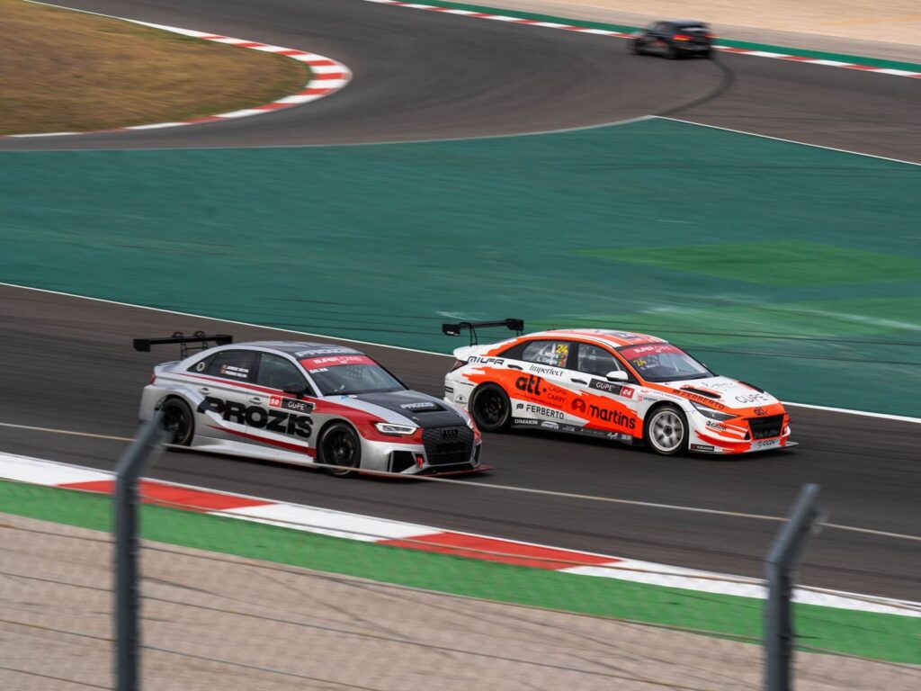 Two racecars compete at high speed on a professional race track, showcasing thrilling motorsport action.