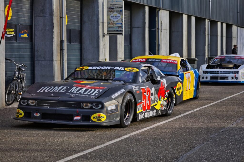 Racing stock cars lined up at a garage in Raceway Venray, showcasing motorsport excitement.