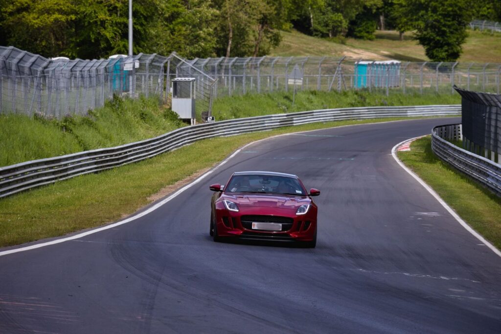 Red sports car on a winding race track at Nürburgring on a sunny day.