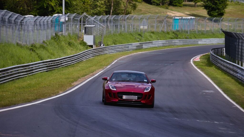 Red sports car on a winding race track at Nürburgring on a sunny day.