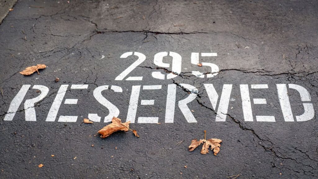 Close-up of a reserved parking spot with fallen leaves on a cracked surface.